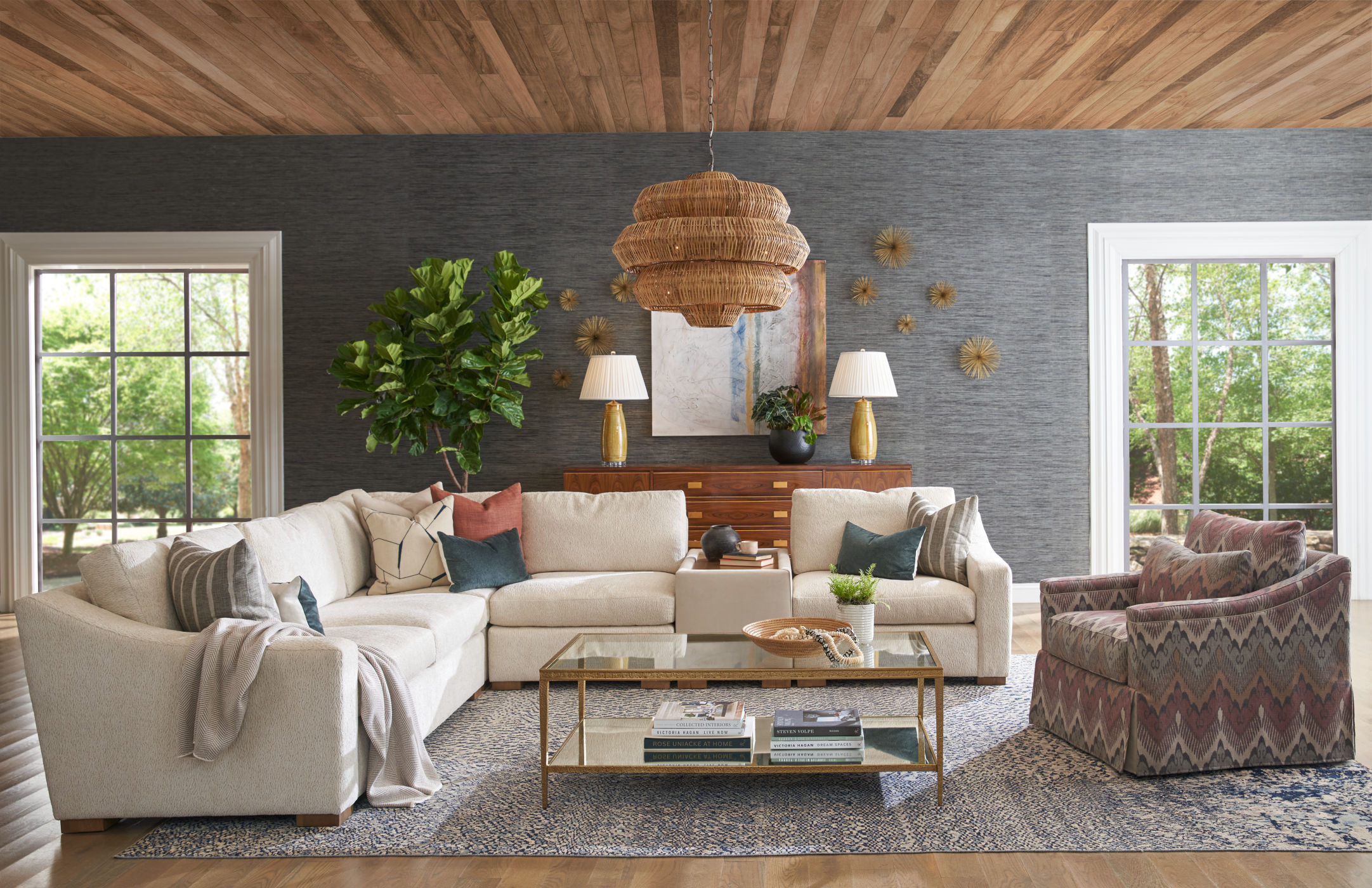 Sunlit living room with a cream sectional, layered pillows, grasscloth walls, and a natural wood ceiling