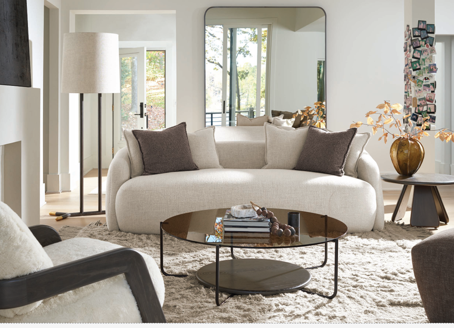 Curved cream sofa with a round cocktail table, layered rug, and a slim floor lamp in an airy living room