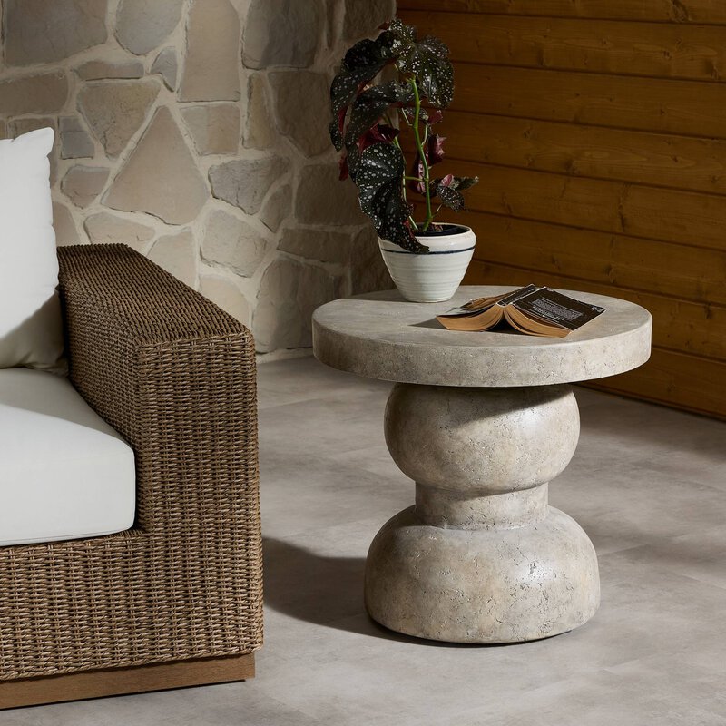 Woven lounge chair beside a stone side table set against a natural stone wall on a quiet patio