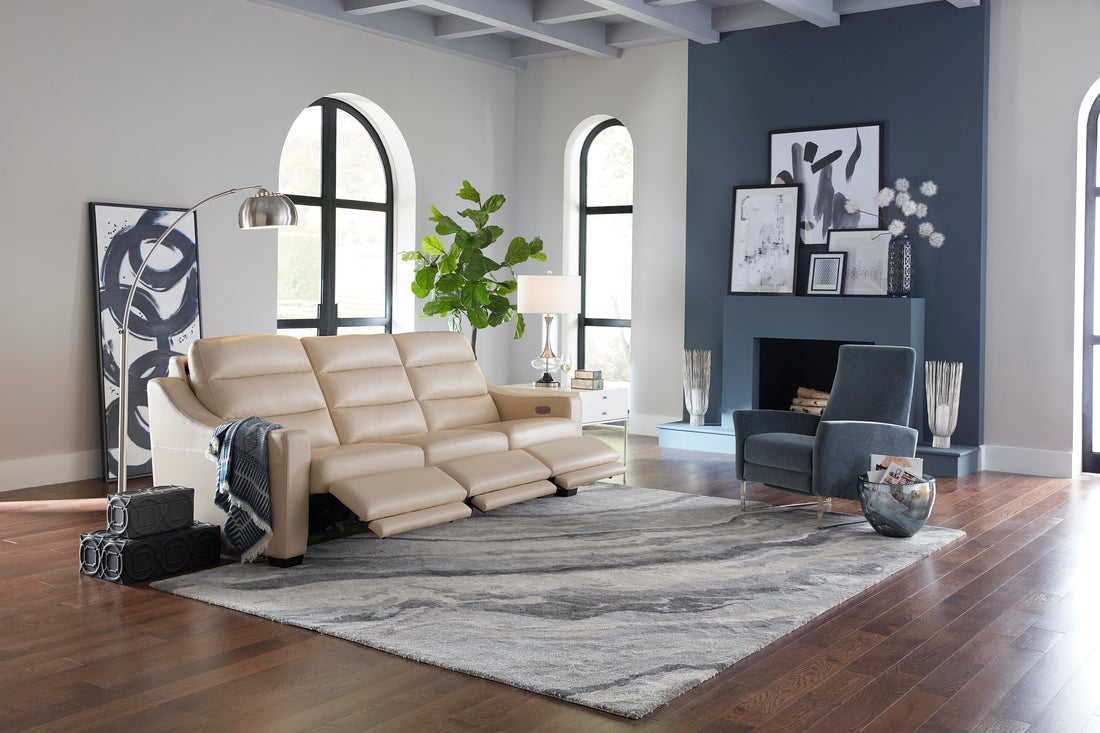 Cream leather reclining sofa with an extended footrest, arc floor lamp, and accent chair in a bright media room